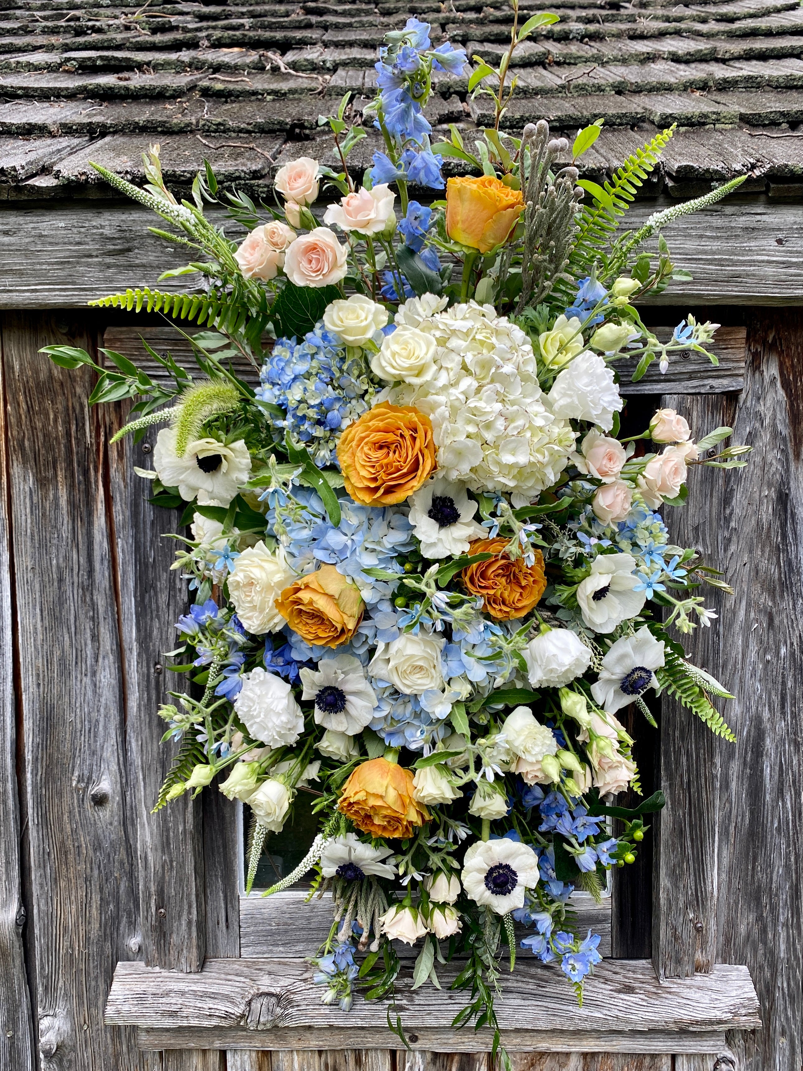 Sympathy arrangement hung on old barn door with blue and white hydrangeas and pops of orange and pinks.