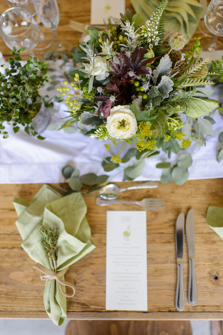 Elegant table setting with floral arrangement, green napkins, and cutlery on a wooden table.